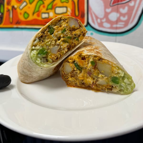 A large, cut breakfast burrito filled with eggs, potatoes, cheese, and green chiles on a white plate.
