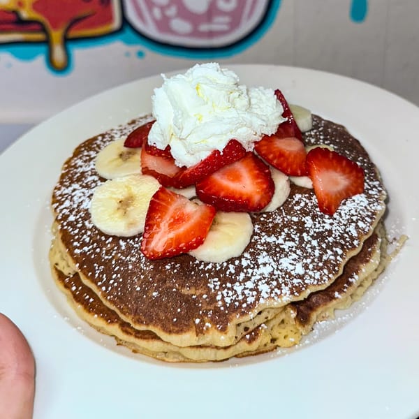 Fluffy pancakes topped with fresh strawberries, banana slices, whipped cream, and powdered sugar.