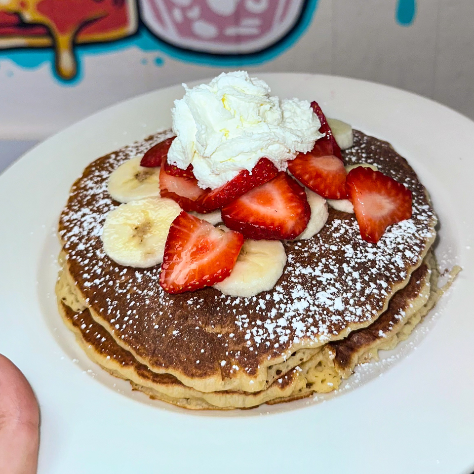 Fluffy pancakes topped with fresh strawberries, banana slices, whipped cream, and powdered sugar.