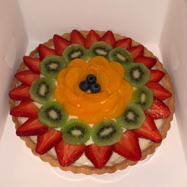 A vibrant fruit tart with strawberries, kiwi, and mandarin oranges arranged in a flower pattern.