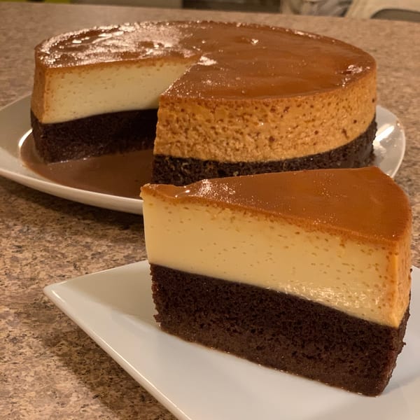 A whole flan cake with a slice removed, showing layers of chocolate cake and creamy flan.