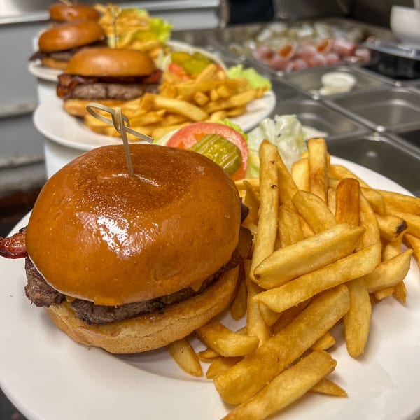 Multiple plates of cheeseburgers with bacon, fries, and a side salad on a white plate.