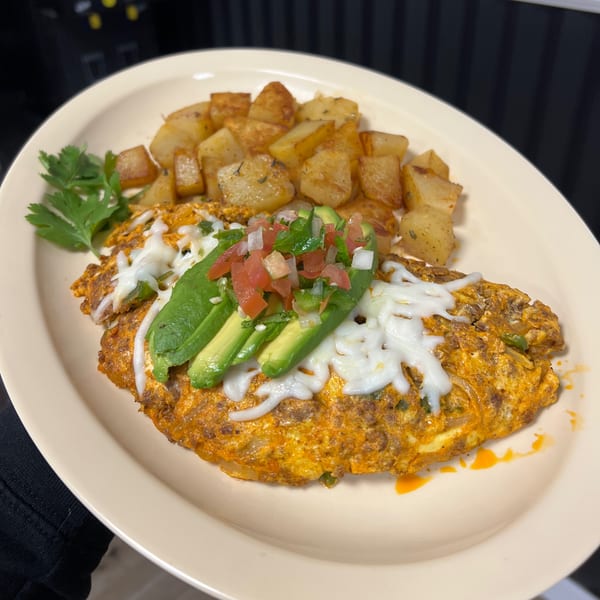 A Mexican omelet with melted cheese, avocado, pico de gallo, and a side of roasted potatoes.