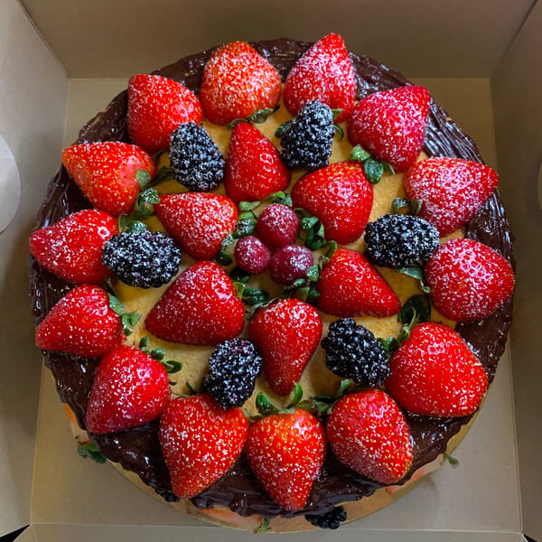 A round cake with chocolate frosting, topped with strawberries, blackberries, and raspberries, dusted with powdered sugar.