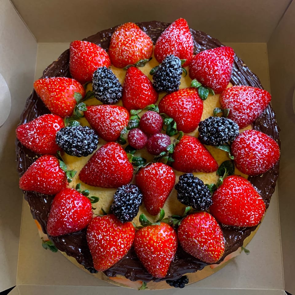 A round cake with chocolate frosting, topped with strawberries, blackberries, and raspberries, dusted with powdered sugar.