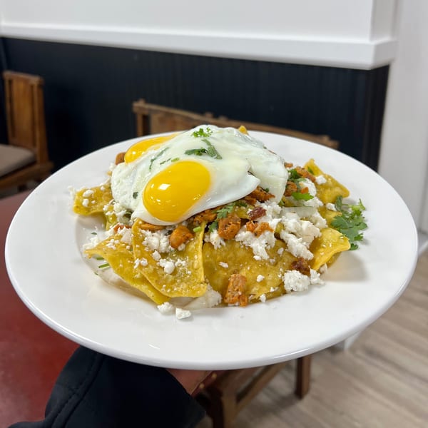 A plate of chilaquiles with two fried eggs, crumbled cheese, and cilantro on a white plate.