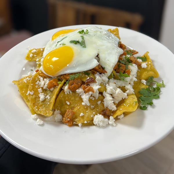 Chilaquiles with two fried eggs, crumbled cheese, and cilantro on a white plate.