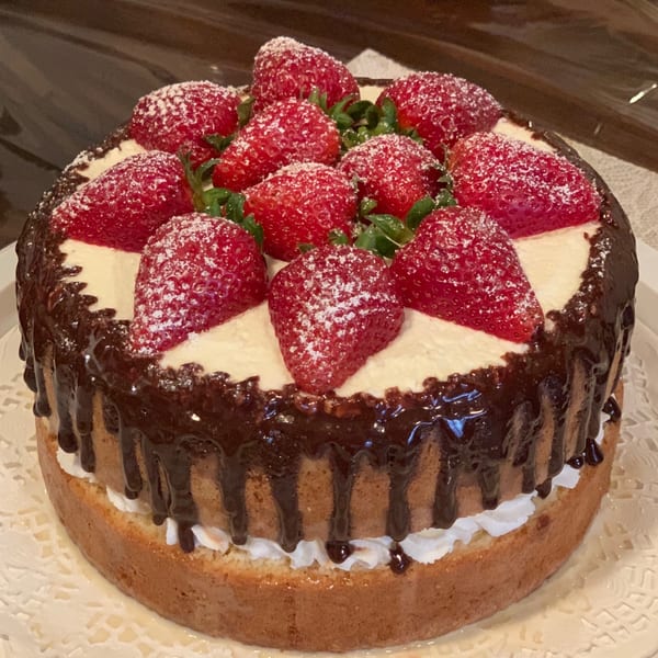 Strawberry cake with chocolate drizzle, whipped cream, and powdered sugar on a white doily.