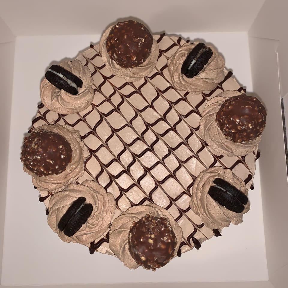 Overhead view of a round cake with chocolate frosting, Ferrero Rocher candies, and Oreo cookies.