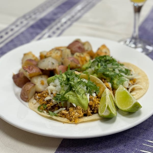 Two Mexican tacos with guacamole, cilantro, and lime, served with roasted potatoes.