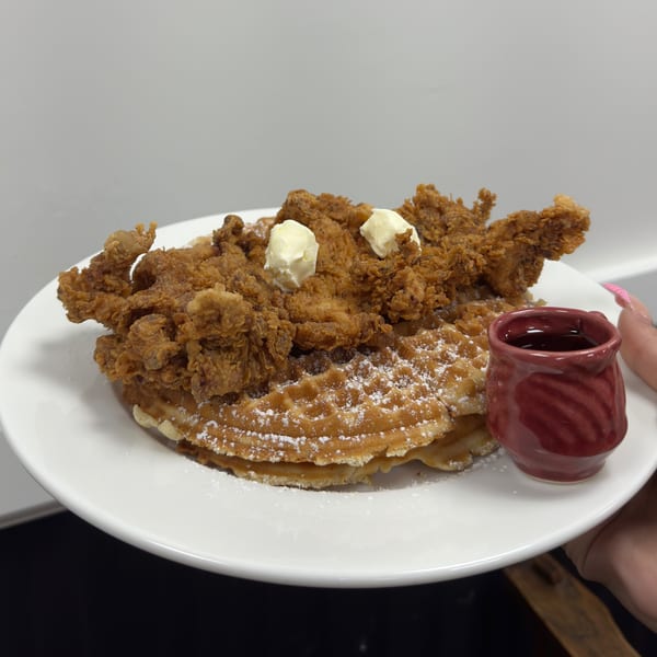 Crispy fried chicken and waffles with butter pats, powdered sugar, and a side of syrup.