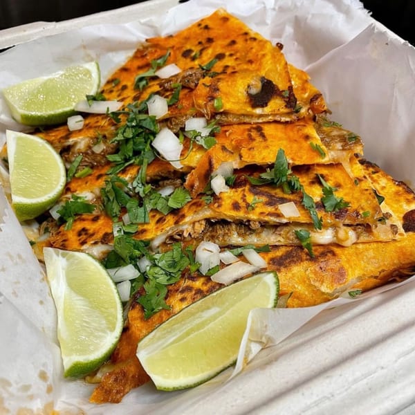 Birria quesadillas from Aquino's Birrieria & Brunch, garnished with cilantro, diced onions, and lime wedges.
