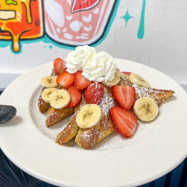 French toast triangles topped with whipped cream, sliced strawberries, and bananas, dusted with powdered sugar.