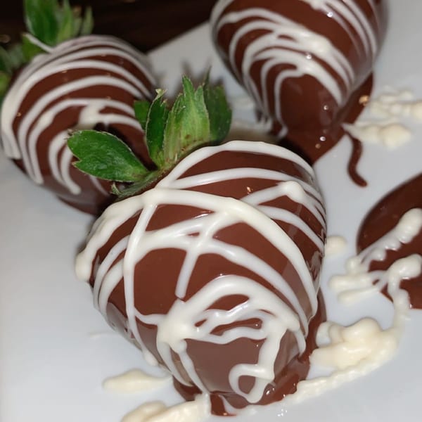 Chocolate-covered strawberries with white drizzle on a white plate, a dessert from Aquino's Birrieria & Brunch.