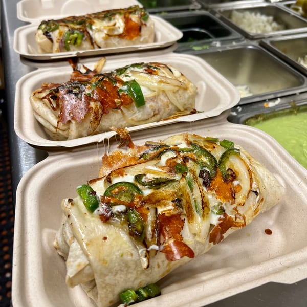 Three cheesy birria burritos with grilled onions and jalapeños in takeout containers at Aquino's Birrieria & Brunch.