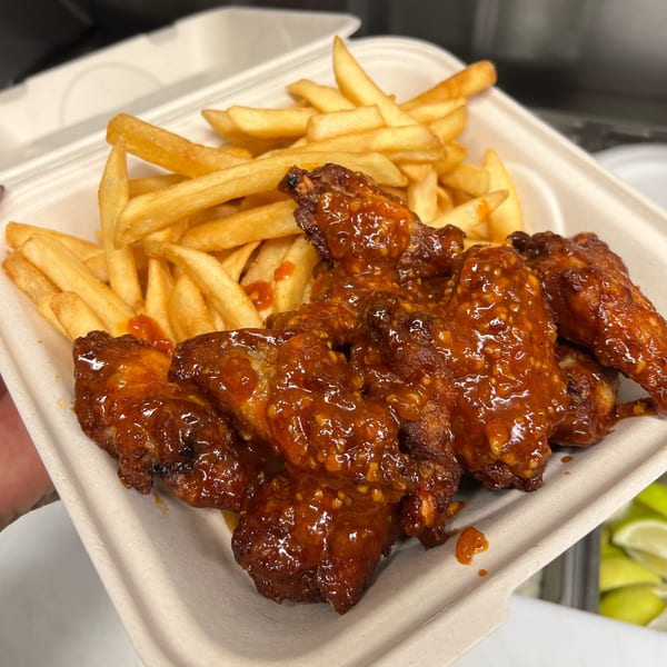 Aquino's Birrieria & Brunch's spicy chicken wings and golden french fries in a takeout container.
