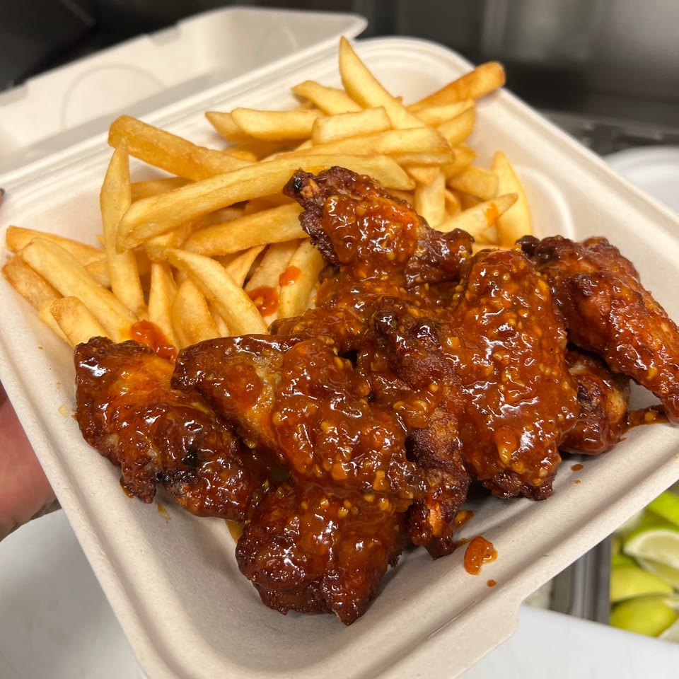 Aquino's Birrieria & Brunch's spicy chicken wings and golden french fries in a takeout container.